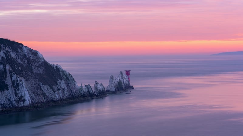 Rock formation with lighthouse at sea during sunset