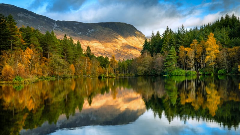 Autumn forest reflected in a calm lake with mountains