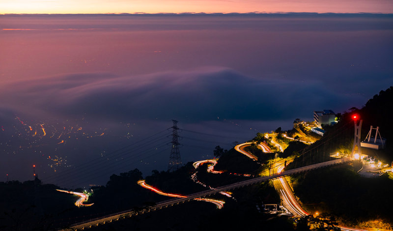 Mountain road with hairpin turns and city lights at dusk