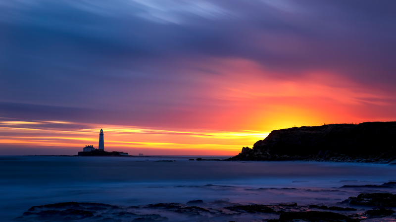 Lighthouse on a rocky island during a colorful sunset
