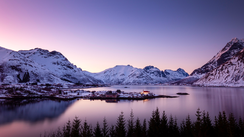 Snowy mountains and a village by the water at dusk