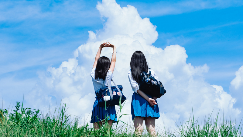 Two schoolgirls stretching outdoors under a cloudy sky