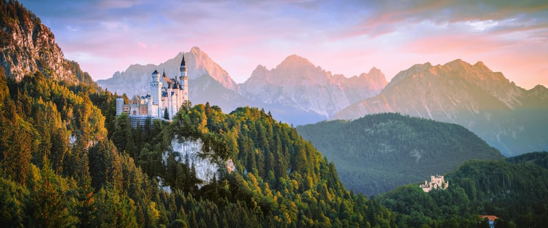 Neuschwanstein Castle on a forested hill with mountains
