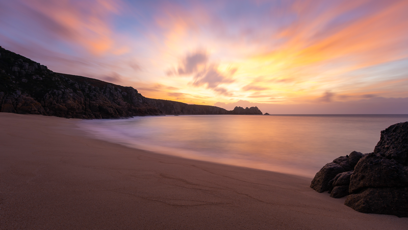 Long exposure sunset over a sandy beach with rocky cliffs