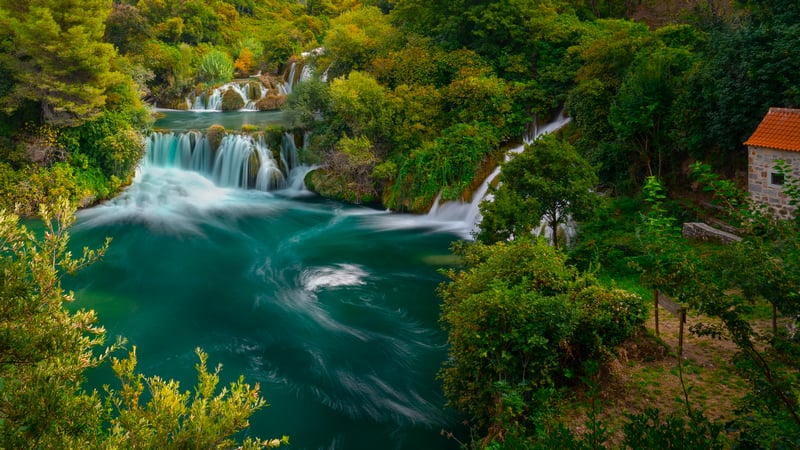 Waterfalls cascade into a turquoise pool surrounded by trees