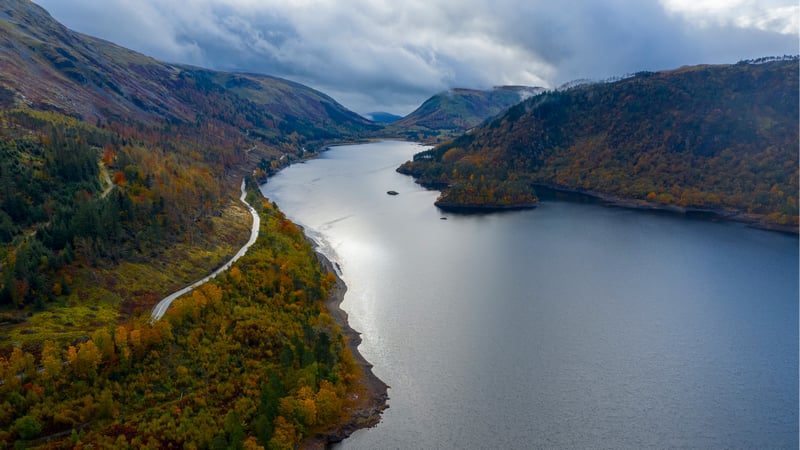 Autumn trees line a winding road next to a large lake