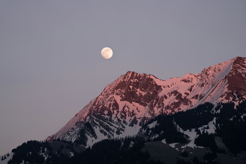 Moon over snow-capped mountains at sunset