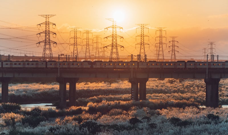 Train crossing bridge with power lines at sunset