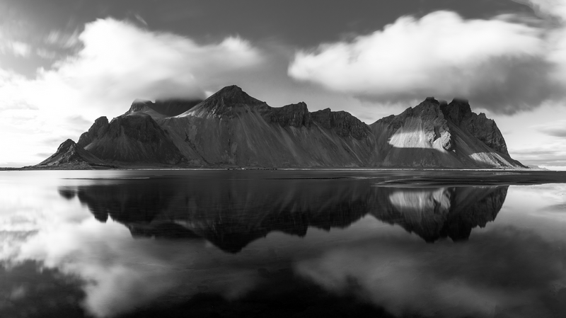 Monochrome mountains reflected in still water under clouds