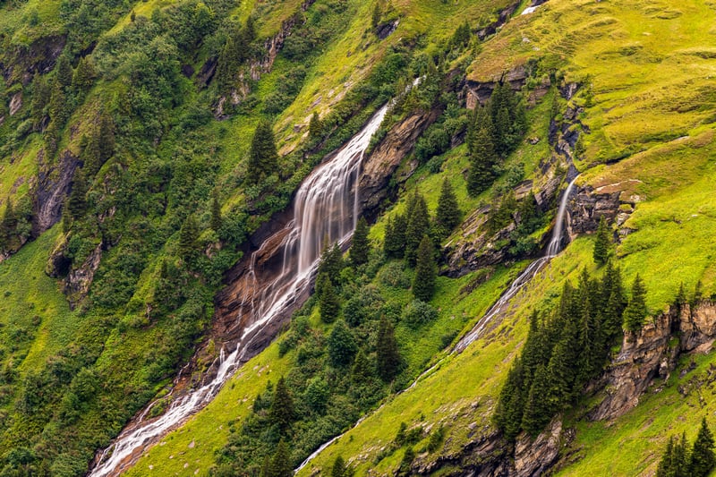 Waterfall cascading down a green mountain slope in Switzerland