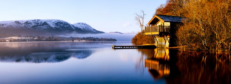 House on a lake with mountains and mist at sunrise