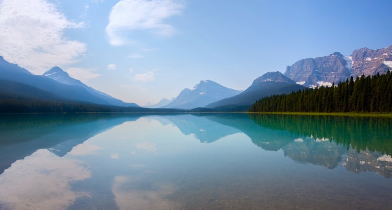 Calm lake reflecting mountains and forest under a blue sky