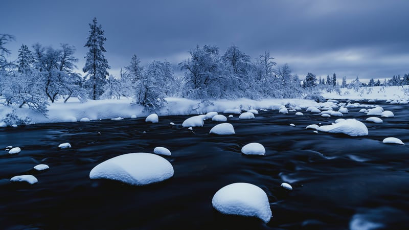 Snow-covered river rocks and trees in winter
