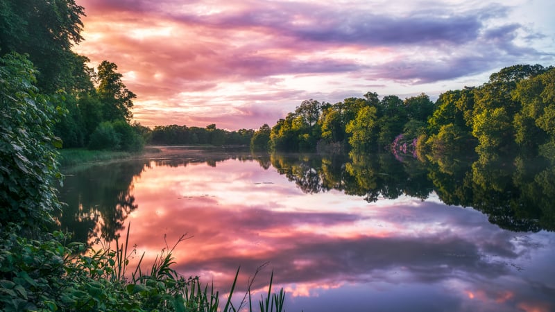 Sunset over a calm river with trees and clouds