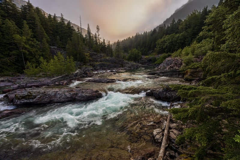 River flowing through a rocky forest with mist at sunset