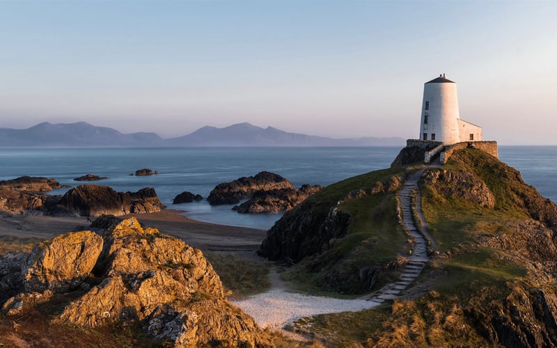 White lighthouse on a rocky island coast with hills in background