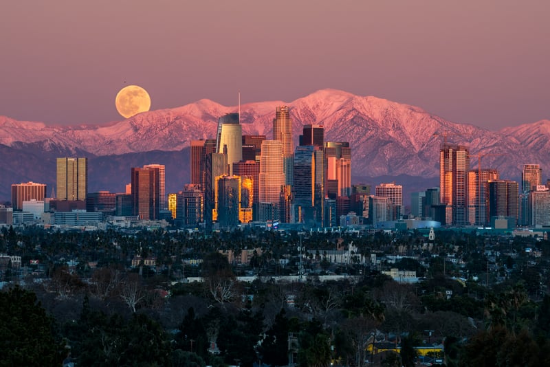 Los Angeles cityscape with moon and snow-capped mountains