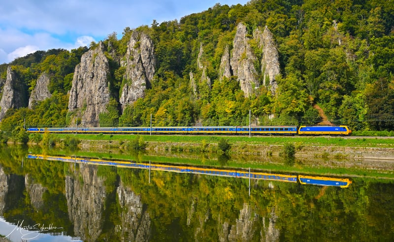Train traveling along a river with rocky cliffs