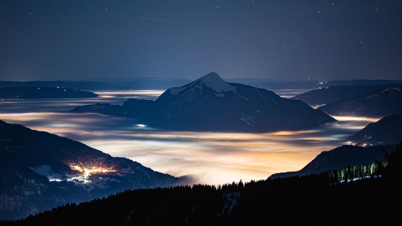Mountain peak above mist and city lights at night