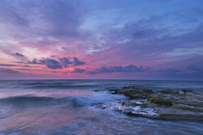 Rocky Coastline with Waves Under Purple Sunset Sky