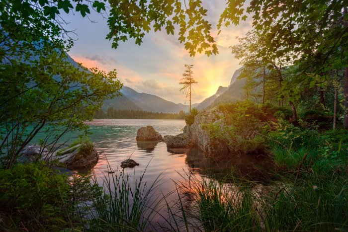 Scenic mountain lake at sunset framed by green trees