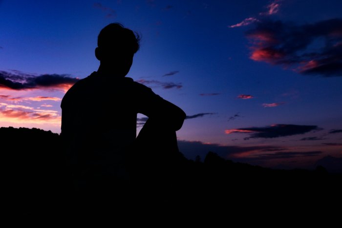 Silhouette of a man sitting under a twilight sky
