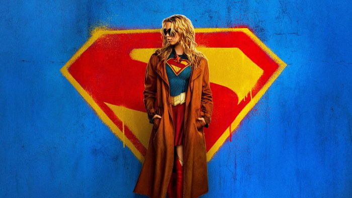 Supergirl wearing a trench coat in front of her logo
