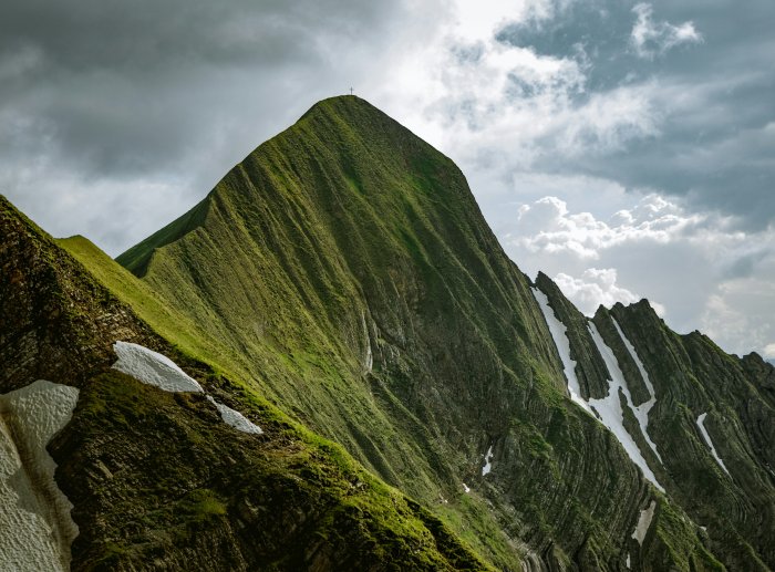 Green Mountain Peak with Summit Cross under Cloudy Sky