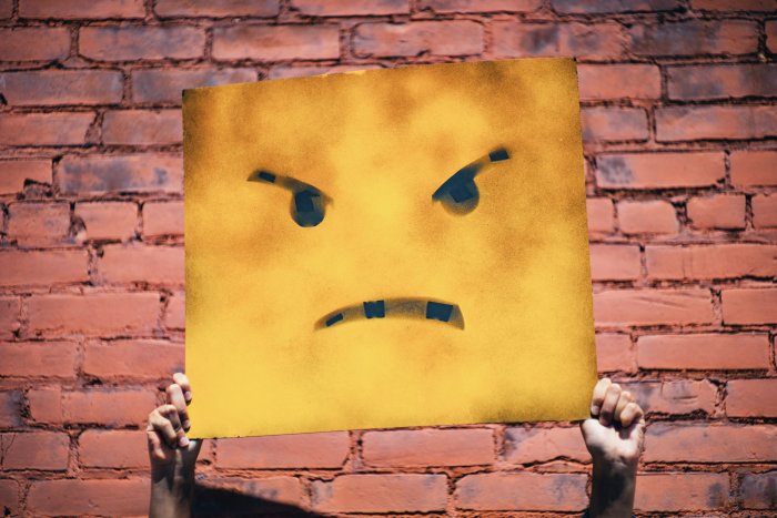 Hands holding an angry yellow face sign
