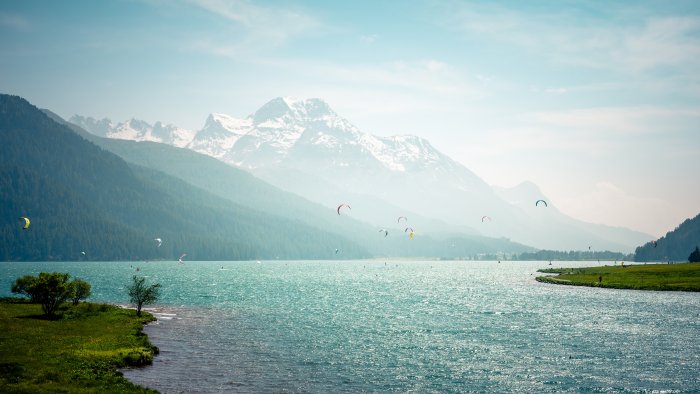 Kitesurfers on a turquoise alpine lake with mountains