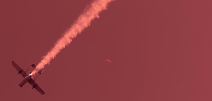Propeller aircraft leaving smoke trail in red sky