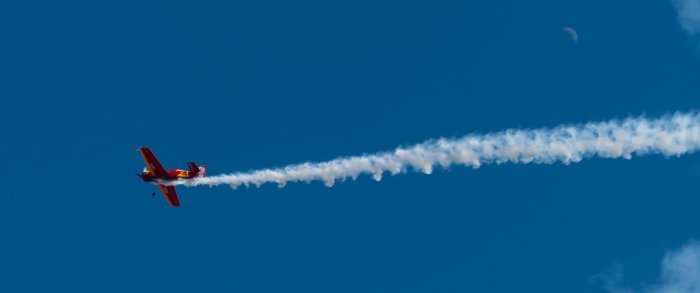 Red stunt plane flying in blue sky with smoke trail
