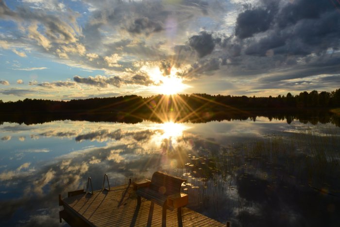 Sunset over calm lake with wooden dock and bench