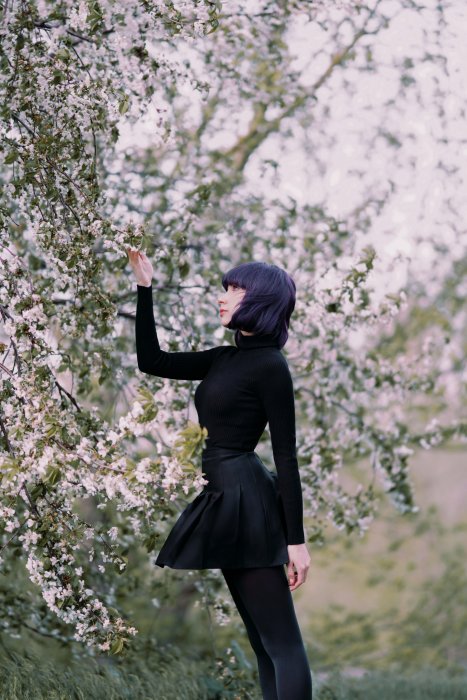 Woman with purple hair in black outfit by blooming tree