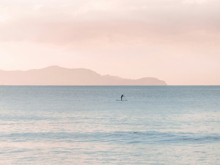 Person paddleboarding on calm sea under pastel sky