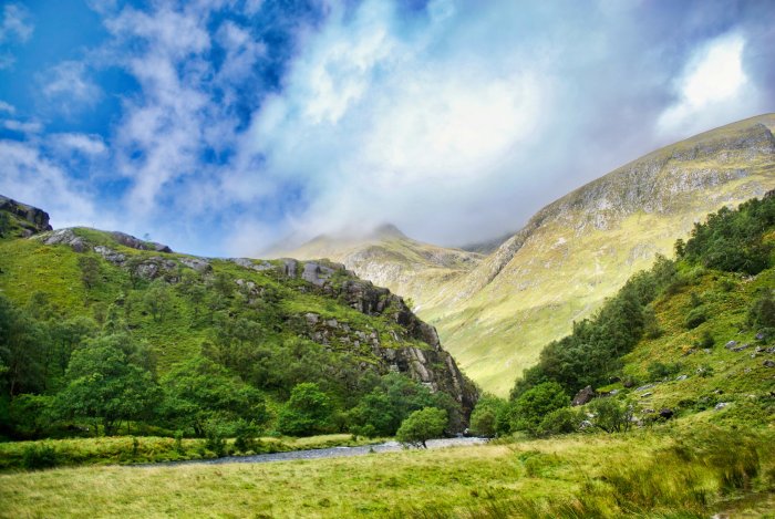 Lush green valley with mountains under cloudy sky
