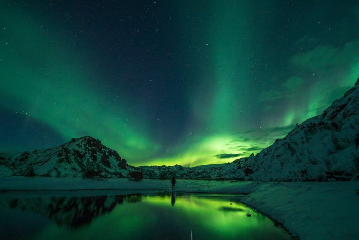 Aurora Borealis over snowy mountains and reflecting water