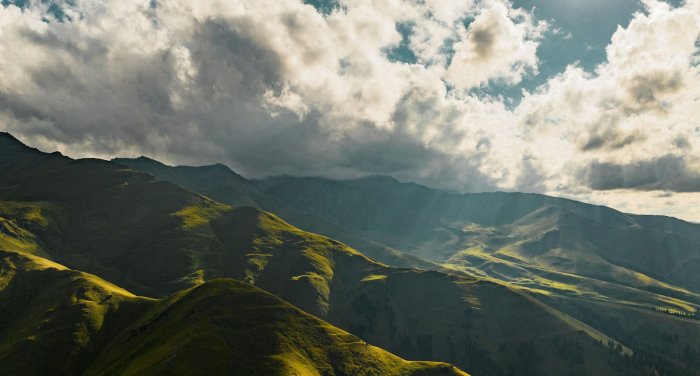 Green rolling hills under a cloudy sky with sunbeams