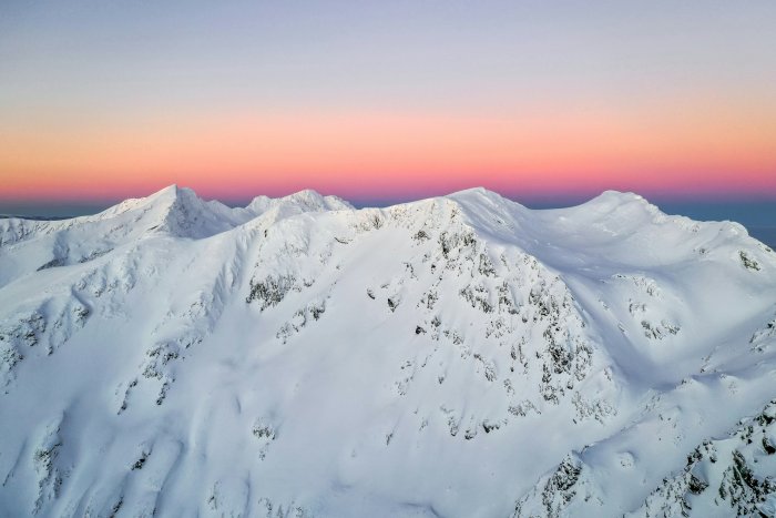 Snowy mountain peaks under a pink sunset sky