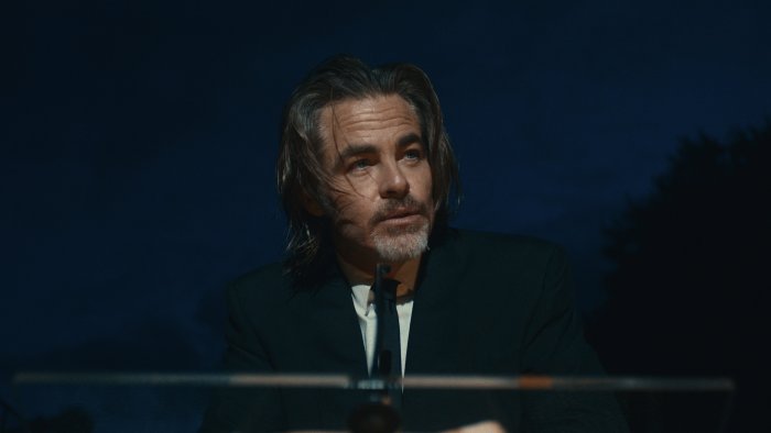 Chris Pine wearing a black suit at a podium