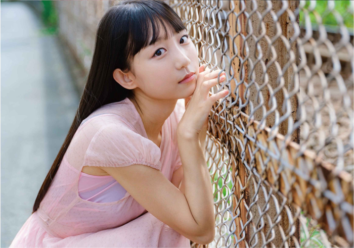 Young Asian Woman in Pink Dress by Chain-Link Fence