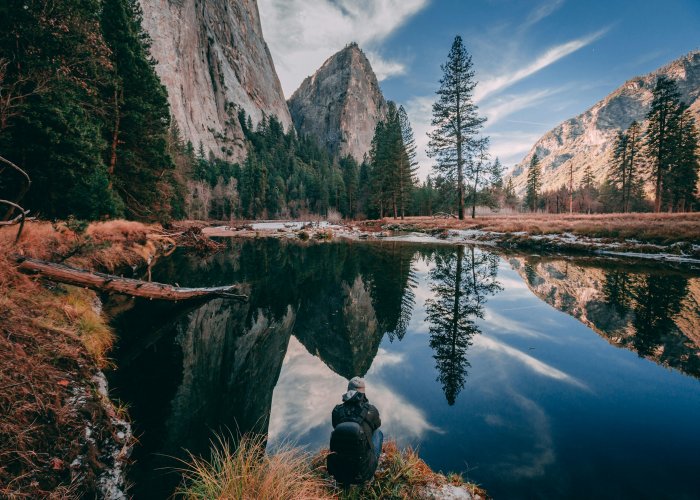 Person sitting by reflective river in Yosemite Valley