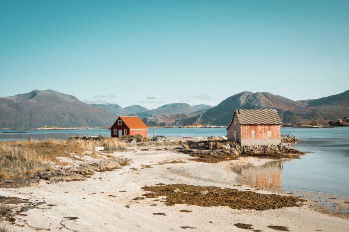 Two wooden cabins on a shoreline with mountains
