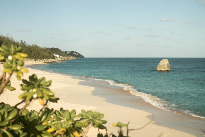 Sandy beach with turquoise ocean water and a lone rock
