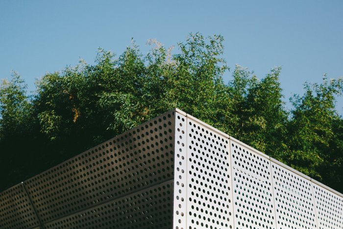 Modern perforated building facade with green trees
