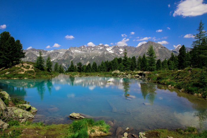 Clear blue alpine lake reflecting mountains and pine trees