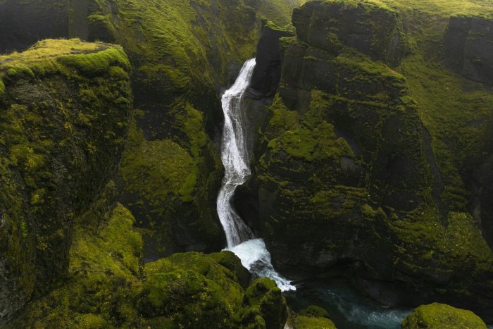 Waterfall flowing through a mossy green canyon
