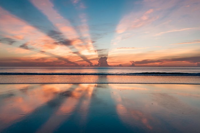 Crepuscular rays reflecting on wet beach sand
