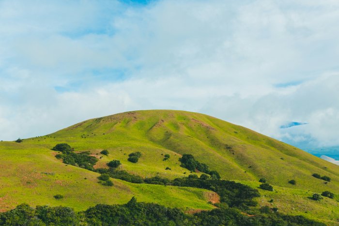 Lush green grassy hill under a cloudy blue sky