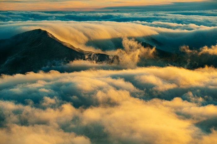 Mountain peak rising above golden clouds at sunset